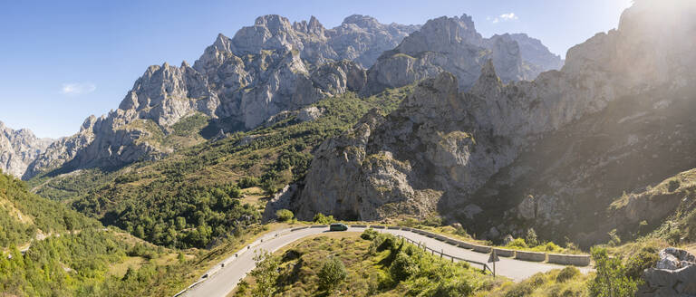 Spain, Castile and Leon, Posada de Valdeon, Panoramic view of Picos de Europa range in summer with asphalt road in foreground - MMPF00527