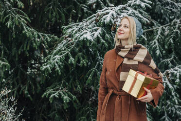 Lächelnde Frau hält Weihnachtsgeschenk-Box vor Tannenbaum mit Schnee - VSNF00149