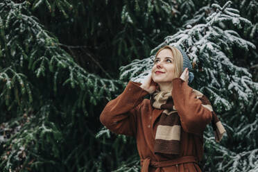 Lächelnde Frau in warmer Kleidung vor einem Tannenbaum - VSNF00150