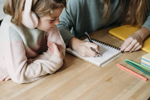 Hand of woman writing on notebook by girl at home - EBBF07250