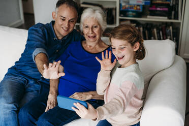 Glückliches Mädchen mit Großmutter und Vater mit Videoanruf auf Handy zu Hause - EBBF07254