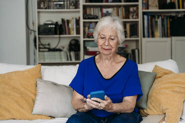 Lächelnde ältere Frau mit Smartphone auf dem Sofa im Wohnzimmer - EBBF07261