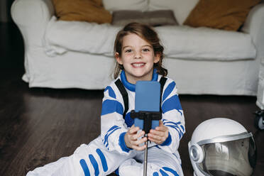 Happy girl wearing space costume with mobile phone in living room - EBBF07286