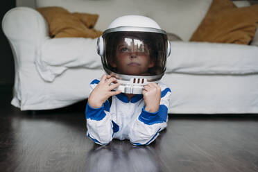 Nachdenkliches Mädchen in Weltraumkostüm und Helm, das zu Hause auf dem Boden liegt - EBBF07292