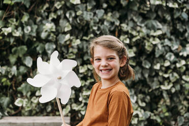 Happy girl with pinwheel toy in front of plant - EBBF07299