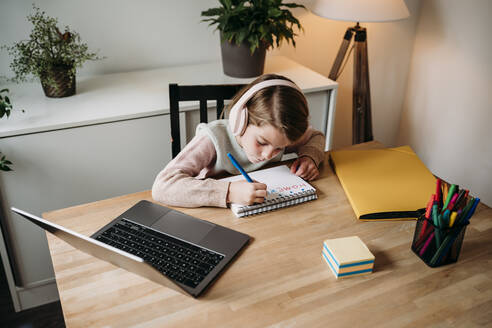 Girl doing homework sitting with laptop on table at home - EBBF07307