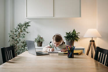 Girl doing homework sitting with laptop at table at home - EBBF07313