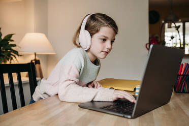 Mädchen mit drahtlosen Kopfhörern und Laptop auf dem Tisch zu Hause - EBBF07315