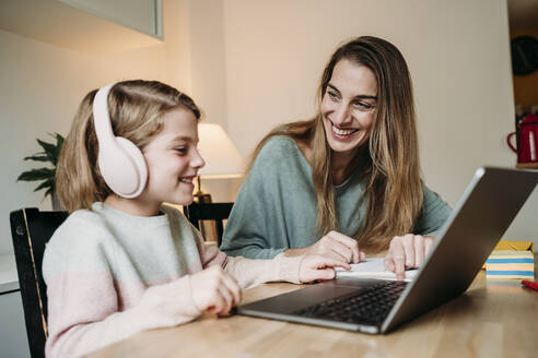 Happy mother helping daughter studying through laptop on table - EBBF07317