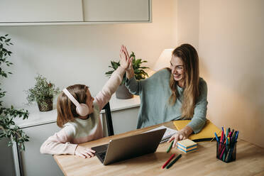 Glückliche Mutter gibt ihrer Tochter, die mit einem Laptop am Tisch sitzt, ein High-Five - EBBF07318