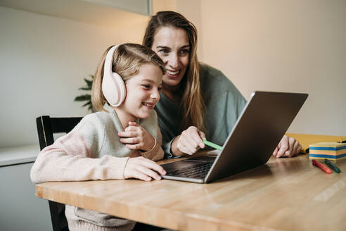 Smiling mother helping daughter e-learning through laptop on table - EBBF07320