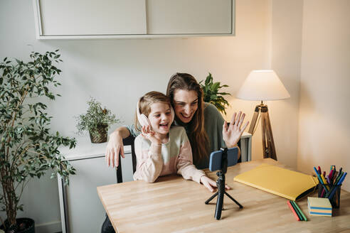 Happy daughter with mother having video call on mobile phone at home - EBBF07327