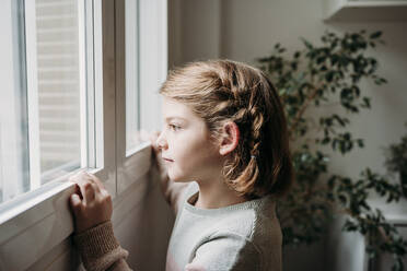 Nachdenkliches Mädchen schaut durch das Fenster zu Hause - EBBF07329