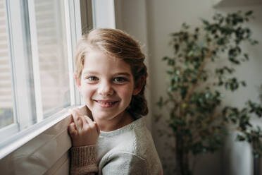 Glückliches süßes Mädchen am Fenster zu Hause - EBBF07331