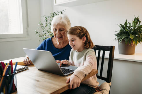 Grandmother helping granddaughter e-learning through laptop at home - EBBF07333