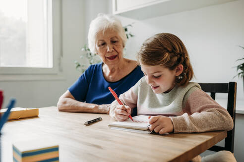 Grandmother helping girl in study on table at home - EBBF07341