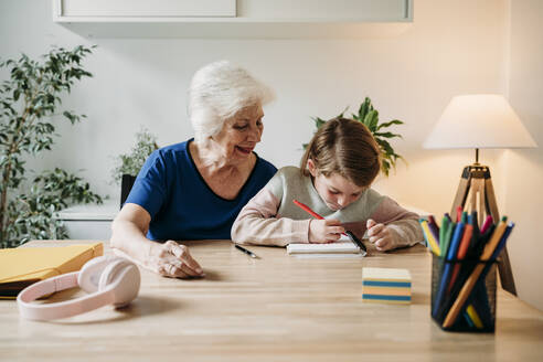 Smiling grandmother helping girl in study on table at home - EBBF07342