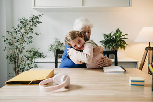Happy girl embracing grandmother at home - EBBF07343