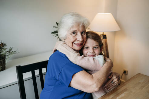 Lächelnde ältere Frau, die ihre Enkelin zu Hause umarmt - EBBF07344