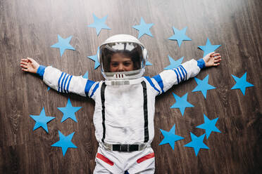 Glückliches Mädchen im Weltraumkostüm auf dem Boden liegend mit blauen Sternen zu Hause - EBBF07349