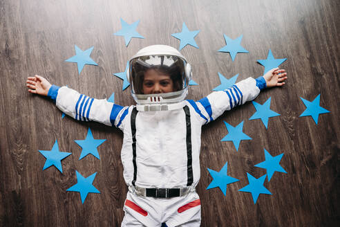 Happy girl wearing space costume lying on floor with blue stars at home - EBBF07349