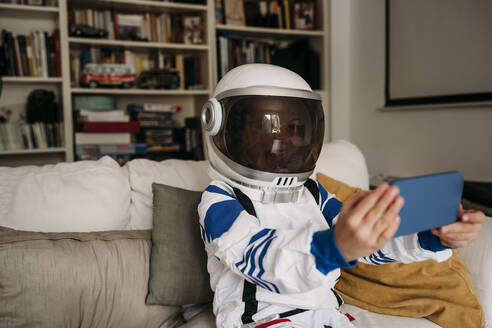 Girl wearing space costume having video call on mobile phone at home - EBBF07355