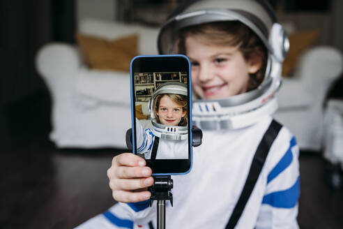 Smiling girl wearing space costume taking selfie through mobile phone at home - EBBF07367