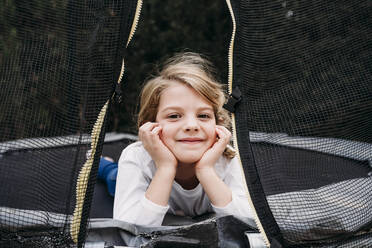 Lächelndes süßes Mädchen liegt auf Trampolin im Garten - EBBF07371