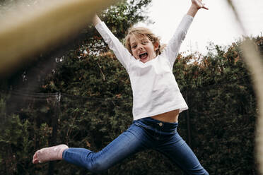 Playful girl with arms raised jumping in garden - EBBF07373