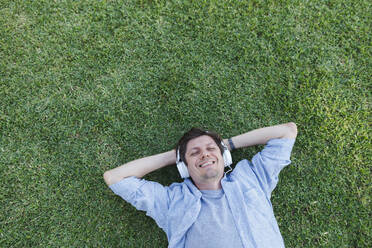 Glücklicher Mann, der sich im Gras entspannt und über Kopfhörer Musik hört - TYF00473