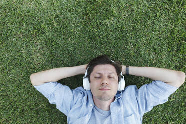 Man listening to music through headphones and relaxing in grass - TYF00474