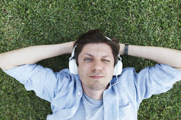 Lächelnder Mann, der über Kopfhörer Musik hört und sich im Gras entspannt - TYF00475