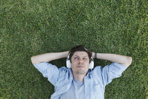 Mann trägt Kopfhörer und entspannt sich im Gras eines Parks - TYF00476