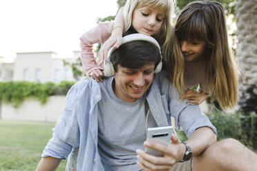 Happy father using smart phone with daughters in park - TYF00478