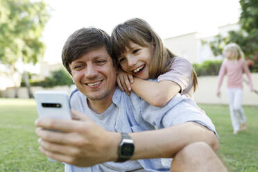 Glückliche Tochter mit Vater bei der Nutzung eines Smartphones im Park - TYF00479