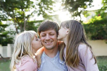 Lächelnder Vater mit Töchtern, die ihn im Park auf die Wange küssen - TYF00481