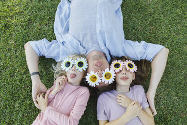 Verspielter Vater und Töchter mit Blumensonnenbrille entspannen sich und haben Spaß im Gras - TYF00484