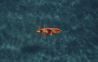 Luftaufnahme von zwei sportlichen Mädchen, die in einem orangefarbenen Kajak auf dem türkisfarbenen Meer in Montepaone, Kalabrien, Italien, paddeln. - AAEF16783