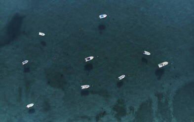 Luftaufnahme einer Gruppe von Schnellbooten, die in Isca sullo Ionio, Kalabrien, Italien, vor Anker liegen, umgeben von einem transparenten blauen Meer. - AAEF16790
