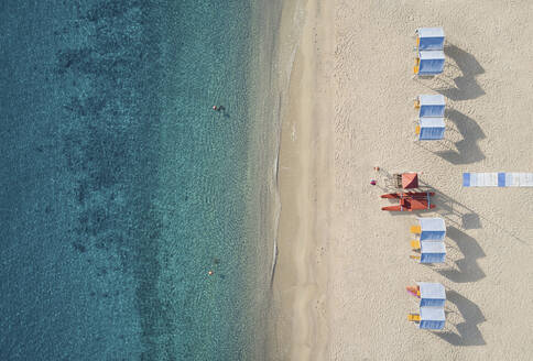 Luftaufnahme einer schönen Küstenlandschaft mit Sandstrand, Pavillons und einem Wachturm am Strandbad vor einem kristallklaren Meer in Kalabrien, Italien. - AAEF16793