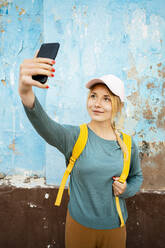 Smiling woman with backpack taking selfie through smart phone - RCPF01544