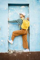 Junge Frau mit gelbem Rucksack an der Wand stehend - RCPF01548