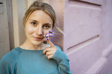 Lächelnde junge Frau mit kleinen Blumen im Gesicht vor einer Wand - RCPF01554