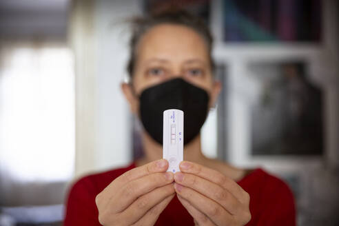 Woman wearing face mask showing her positive Covid-19 rapid test at home - MAMF02312