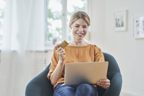Glückliche Frau mit Kreditkarte beim Online-Einkauf über einen Laptop zu Hause - RORF03121