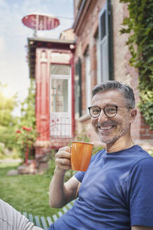 Lächelnder reifer Mann mit Kaffeetasse im Garten - RORF03122