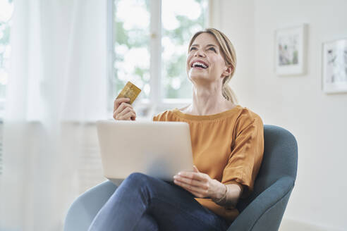 Glückliche Frau mit Kreditkarte beim Online-Shopping mit dem Laptop zu Hause - RORF03124