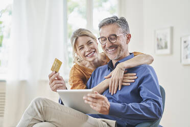 Glückliche Frau umarmt Mann mit Kreditkarte beim Online-Shopping über Tablet-PC zu Hause - RORF03132