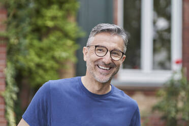 Glücklicher Mann mit Brille vor einem Haus - RORF03136
