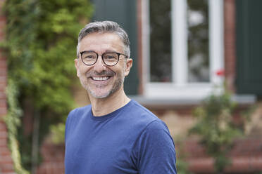 Smiling man wearing eyeglasses in front of house - RORF03137